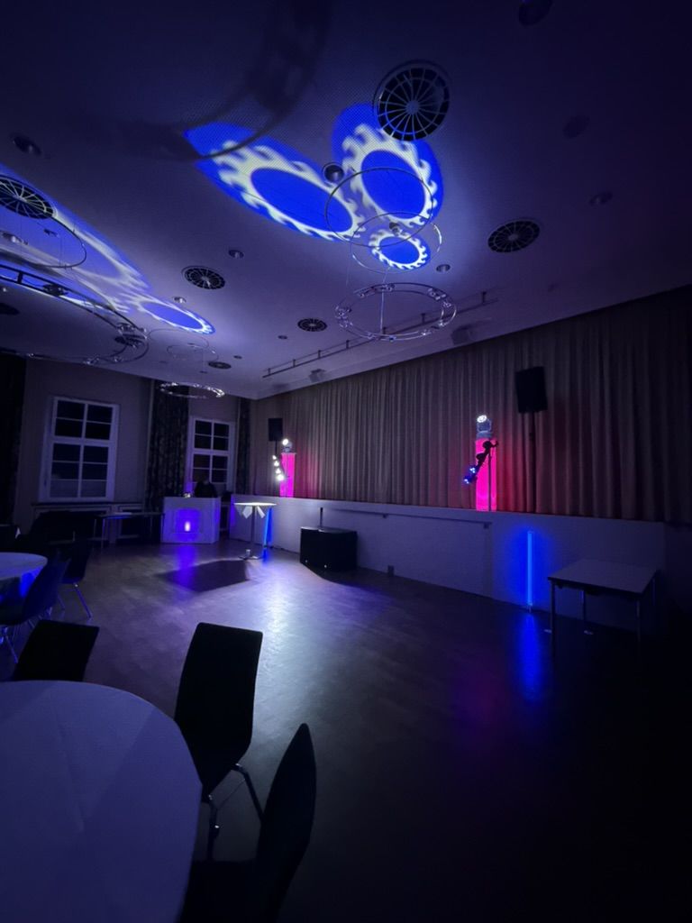 Saal mit blauen Lichtmustern an der Decke und DJ-Pult