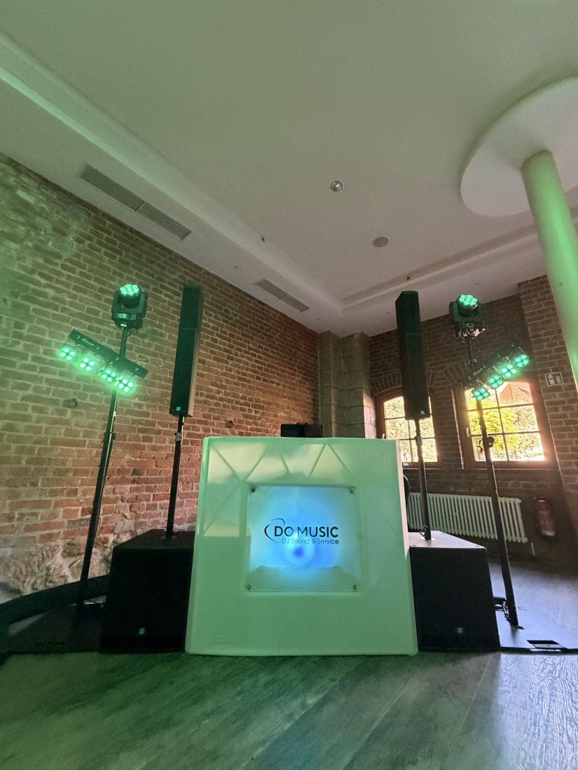 DJ-Pult mit Boxen und Moving Heads in einem Raum mit Bücherregalen