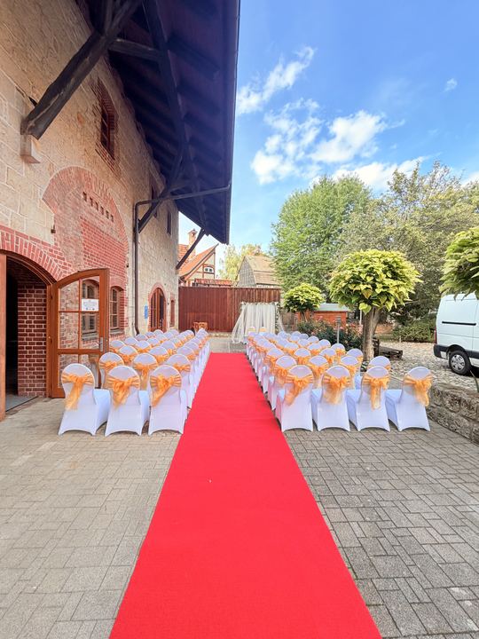 Roter Teppich und weiße Stühle im Innenhof für eine freie Trauung