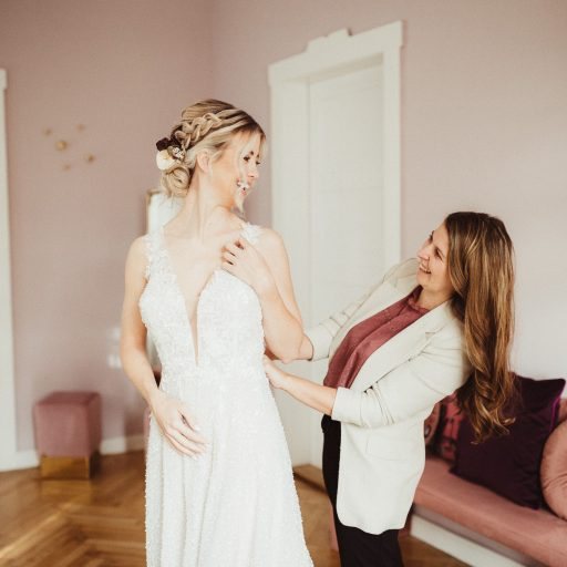 Hochzeitsplanerin richtet vor der Trauung das Kleid der Braut